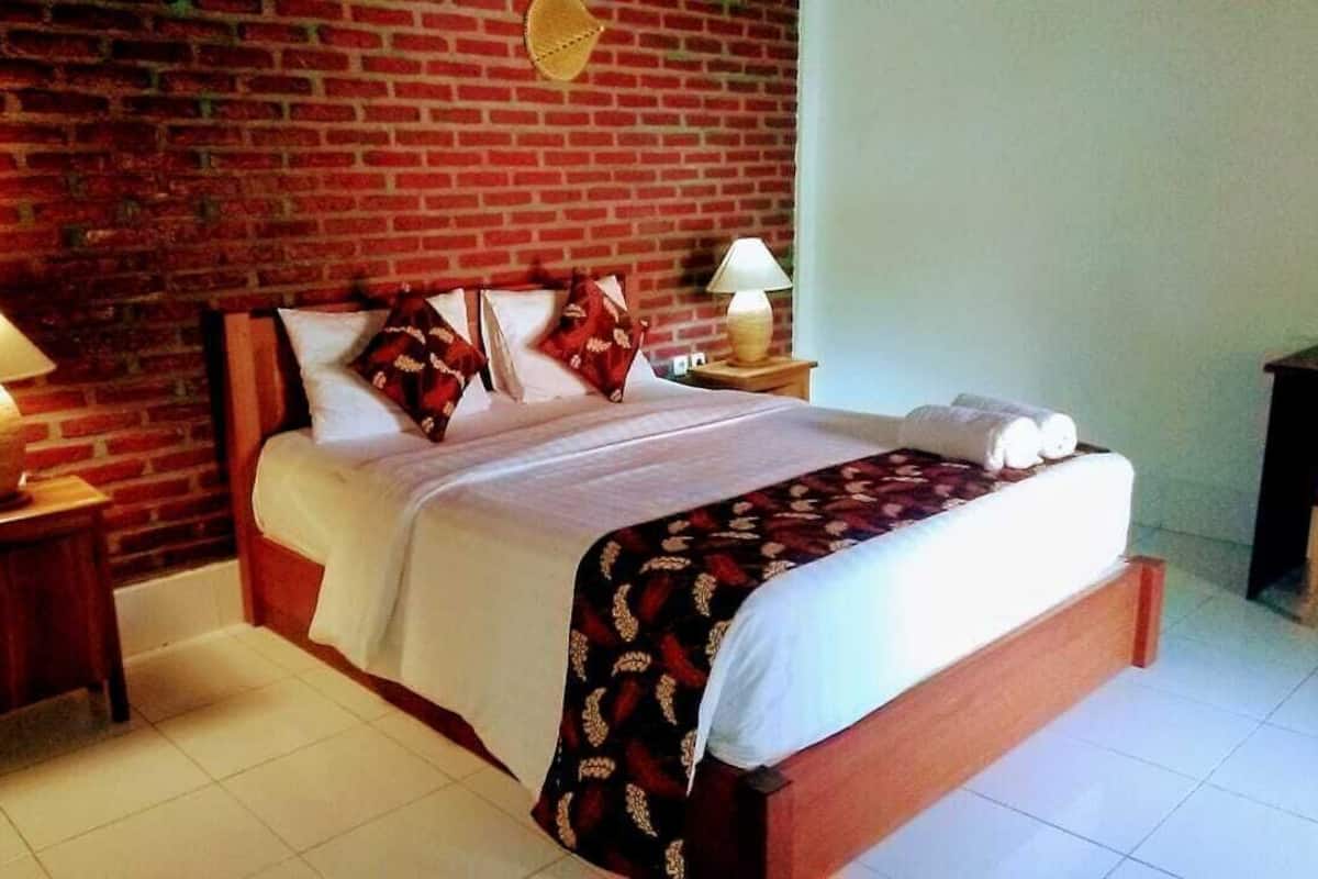 Een kamer met een bakstenen muur, een bed met wit beddengoed, twee bedlampjes en een houten stoel.
