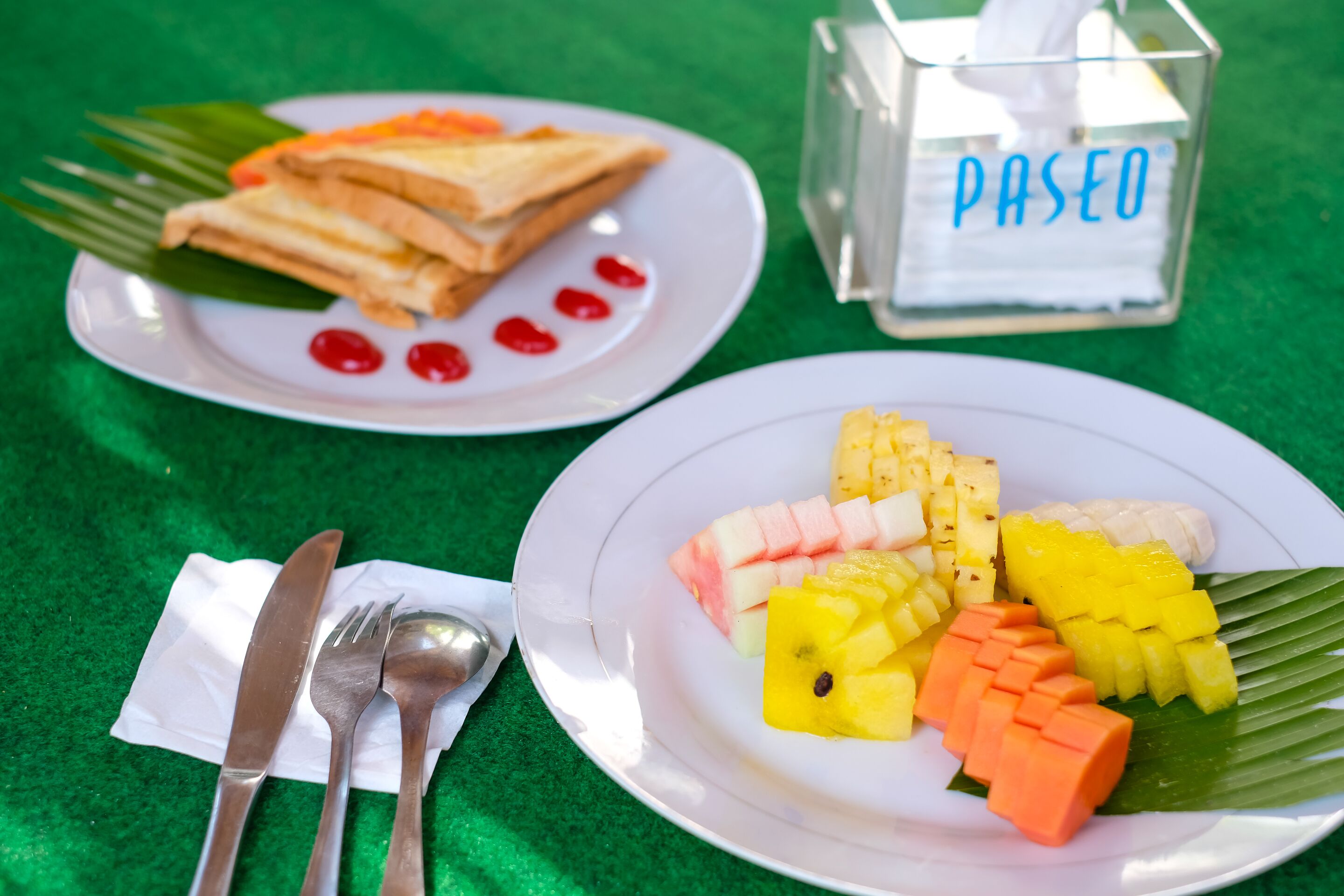 Zwei Teller mit Essen auf einer grünen Tischdecke, einer mit Sandwiches und der andere mit Obst.