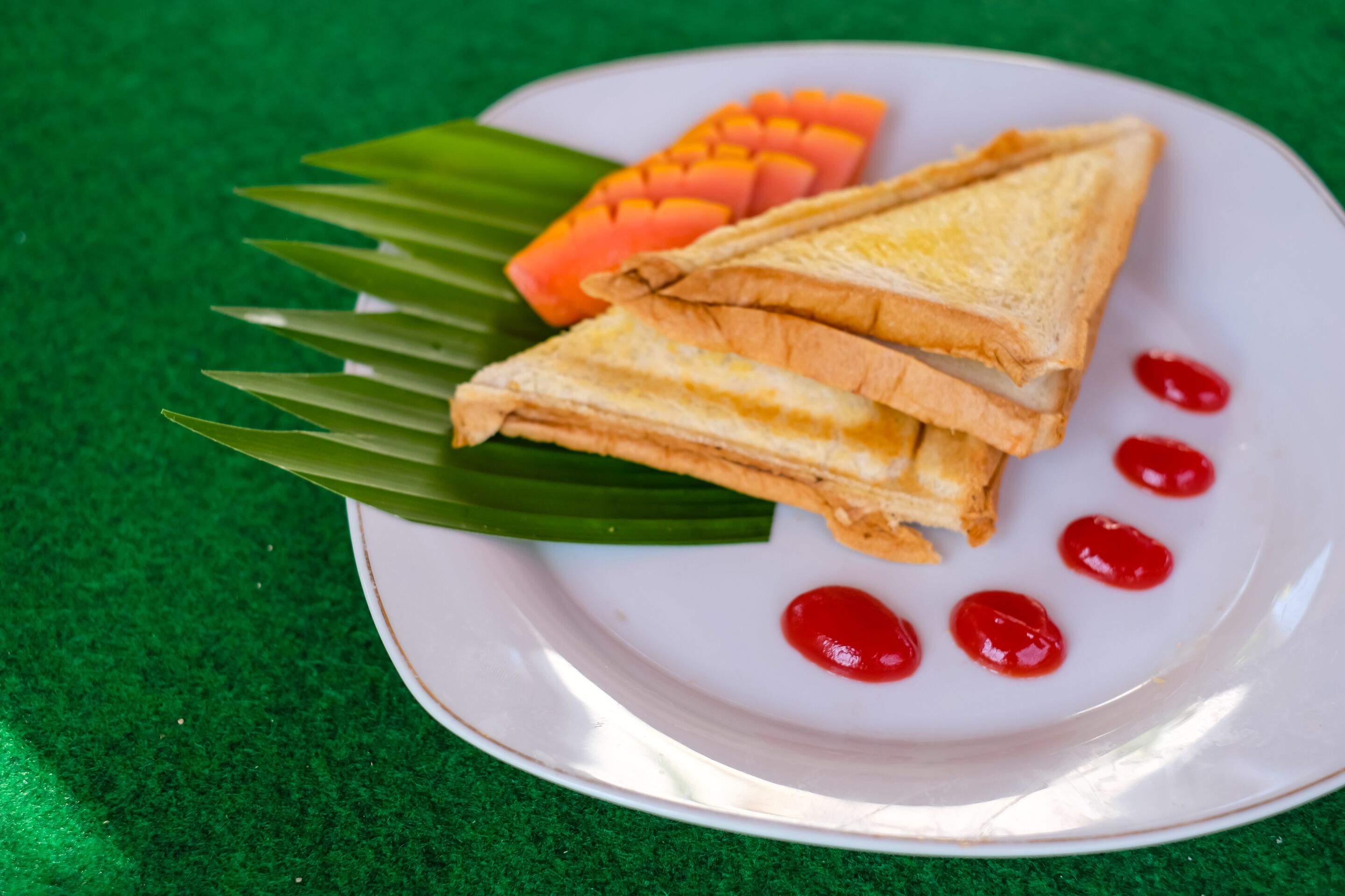 A plate with two sandwiches, mango slices, and red sauce on a white plate with a green background.