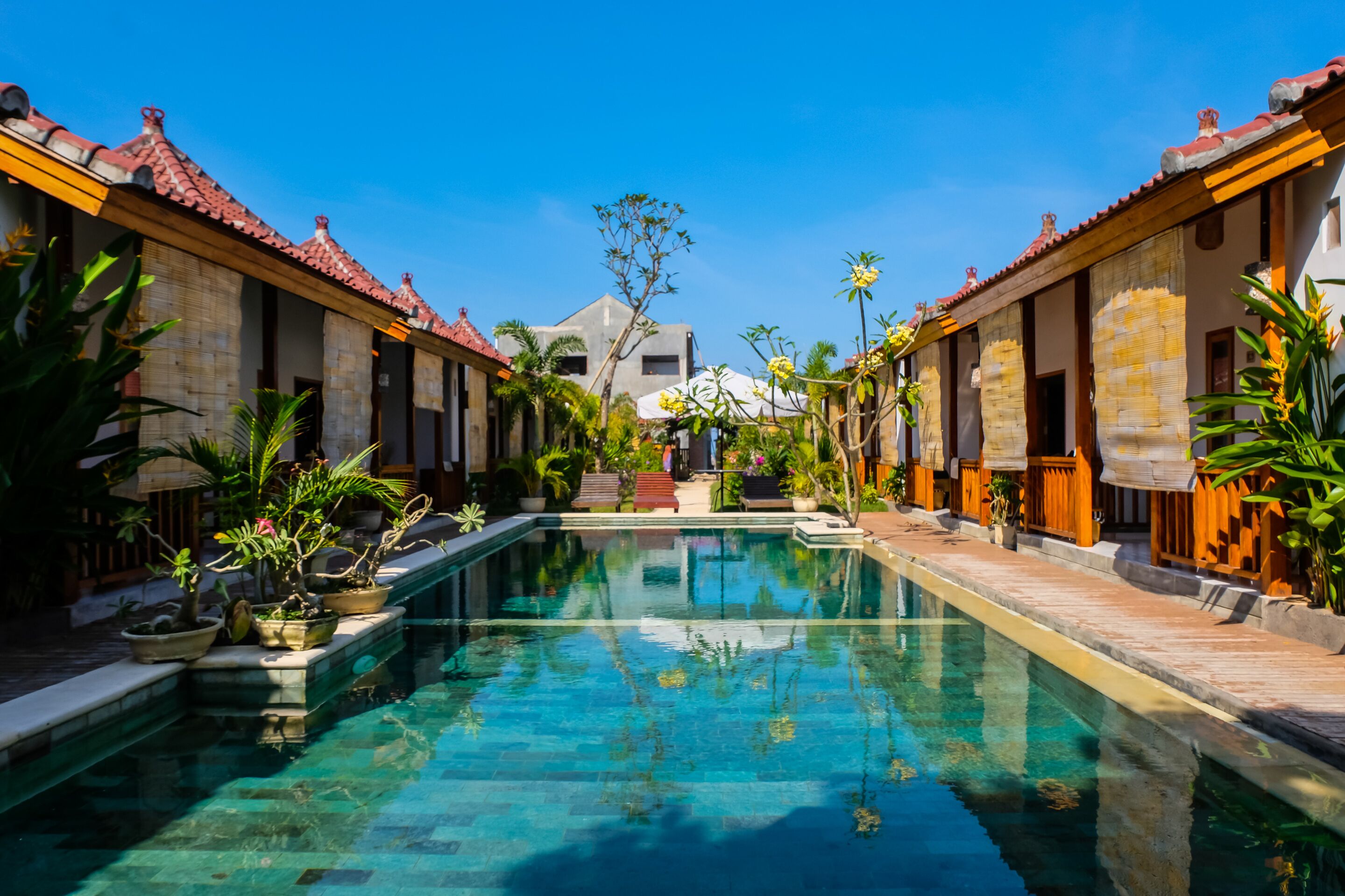 A pool area with clear water, surrounded by buildings with red-tiled roofs and wooden railings.