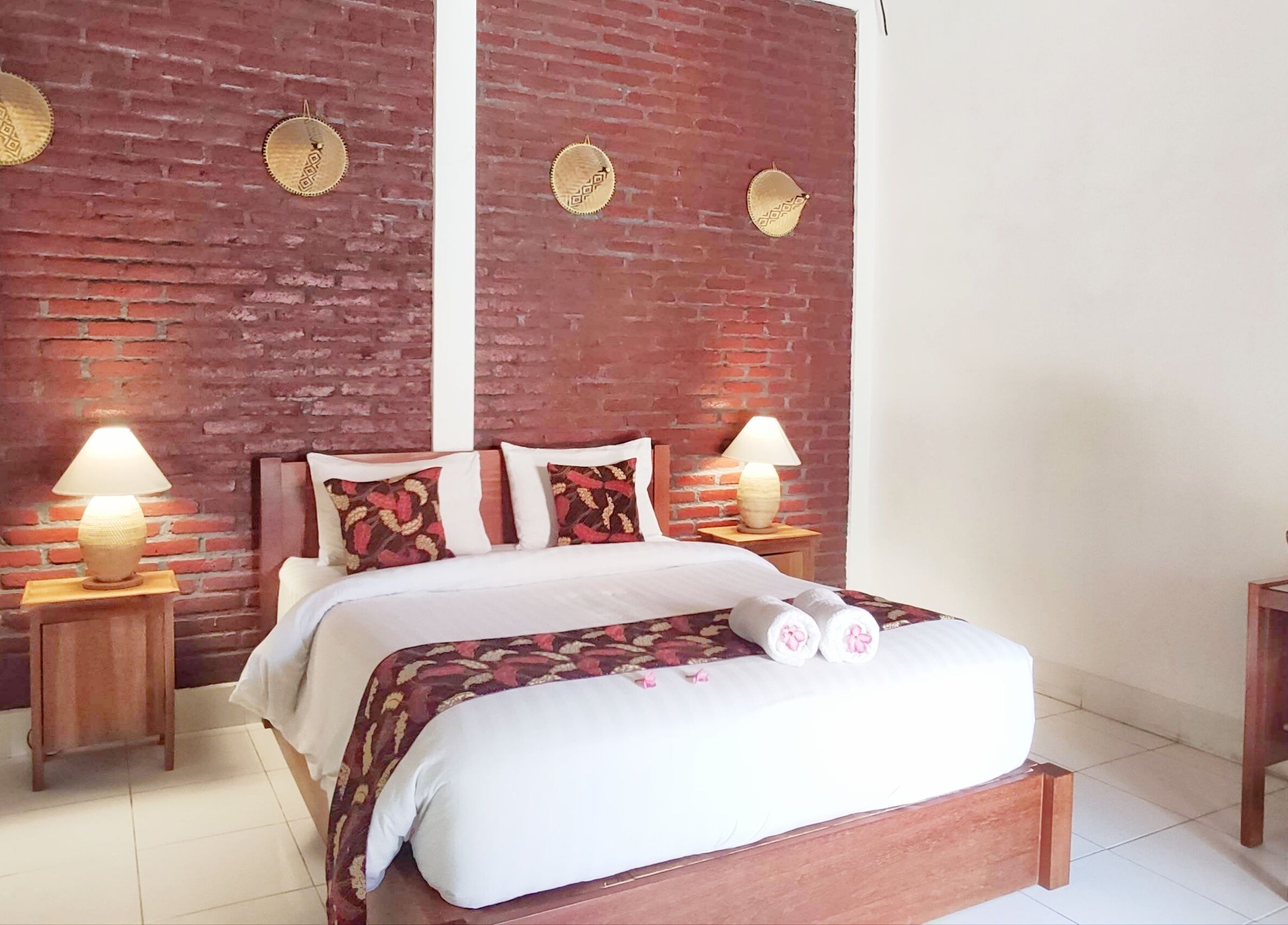 A bed with a wooden headboard, two bedside lamps, and a brick wall with decorative plates.