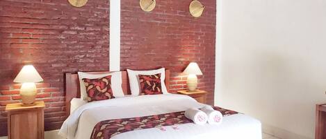 Una cama con cabecera de madera, dos lámparas de noche y una pared de ladrillo con platos decorativos.
