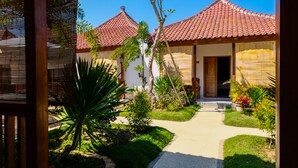 Un sentier mène à un bâtiment traditionnel doté d’un toit en tuiles, entouré d’une végétation luxuriante et d’un petit jardin.
