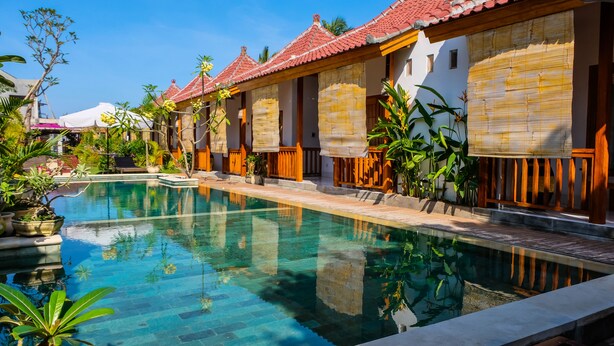 Une piscine entourée de bâtiments de style traditionnel, dotés de toits en tuiles et de stores en bambou.