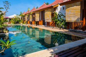 Una piscina rodeada de edificios de estilo tradicional con techos de azulejos y persianas de bambú.