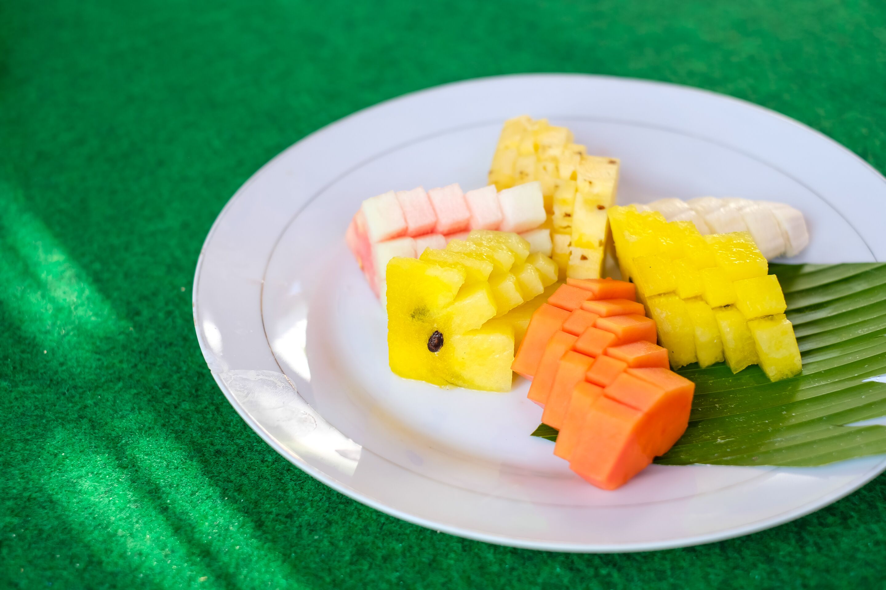 A white plate with various fruits on a green background.