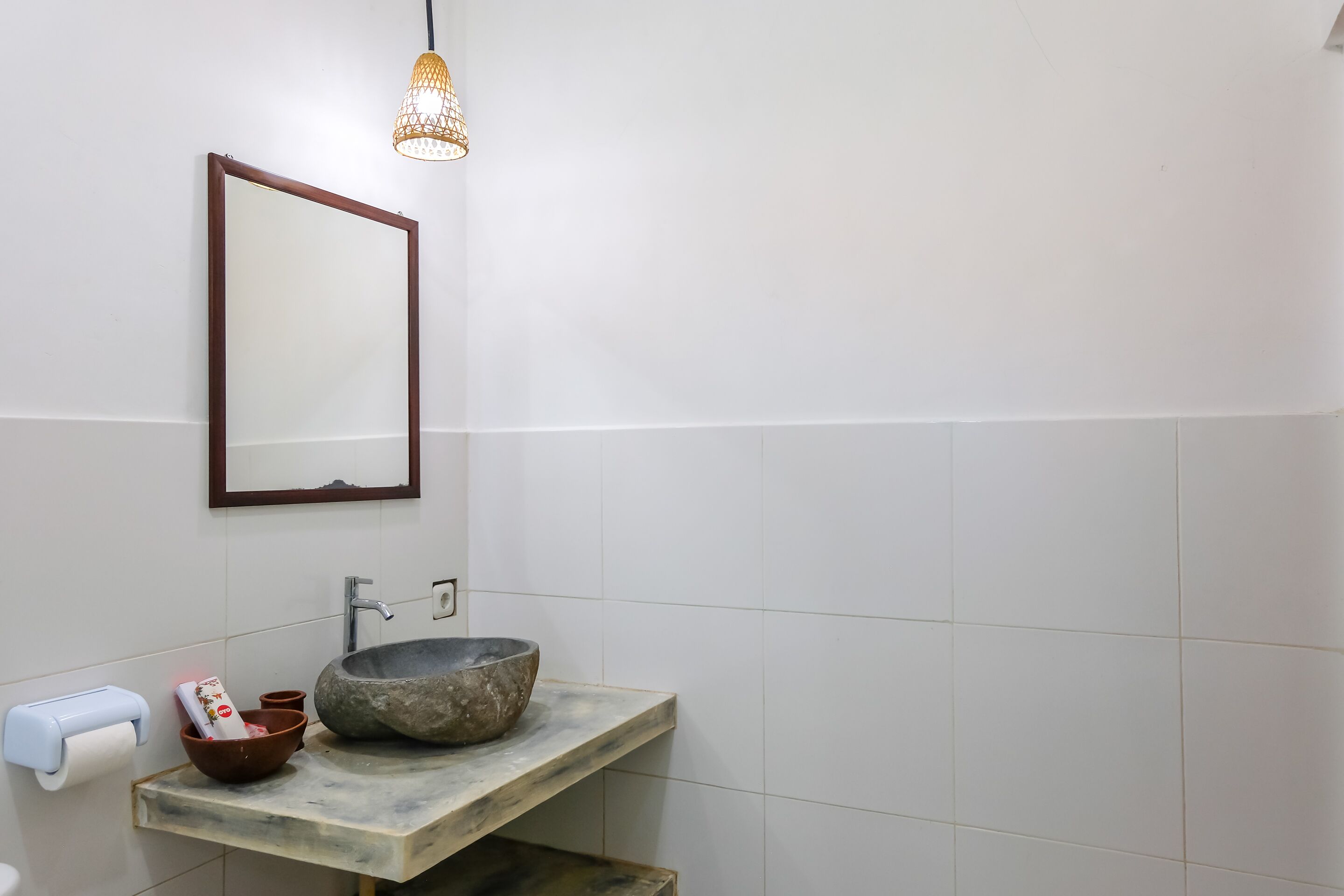A bathroom with a stone sink, a mirror, a towel dispenser, and a hanging light fixture.