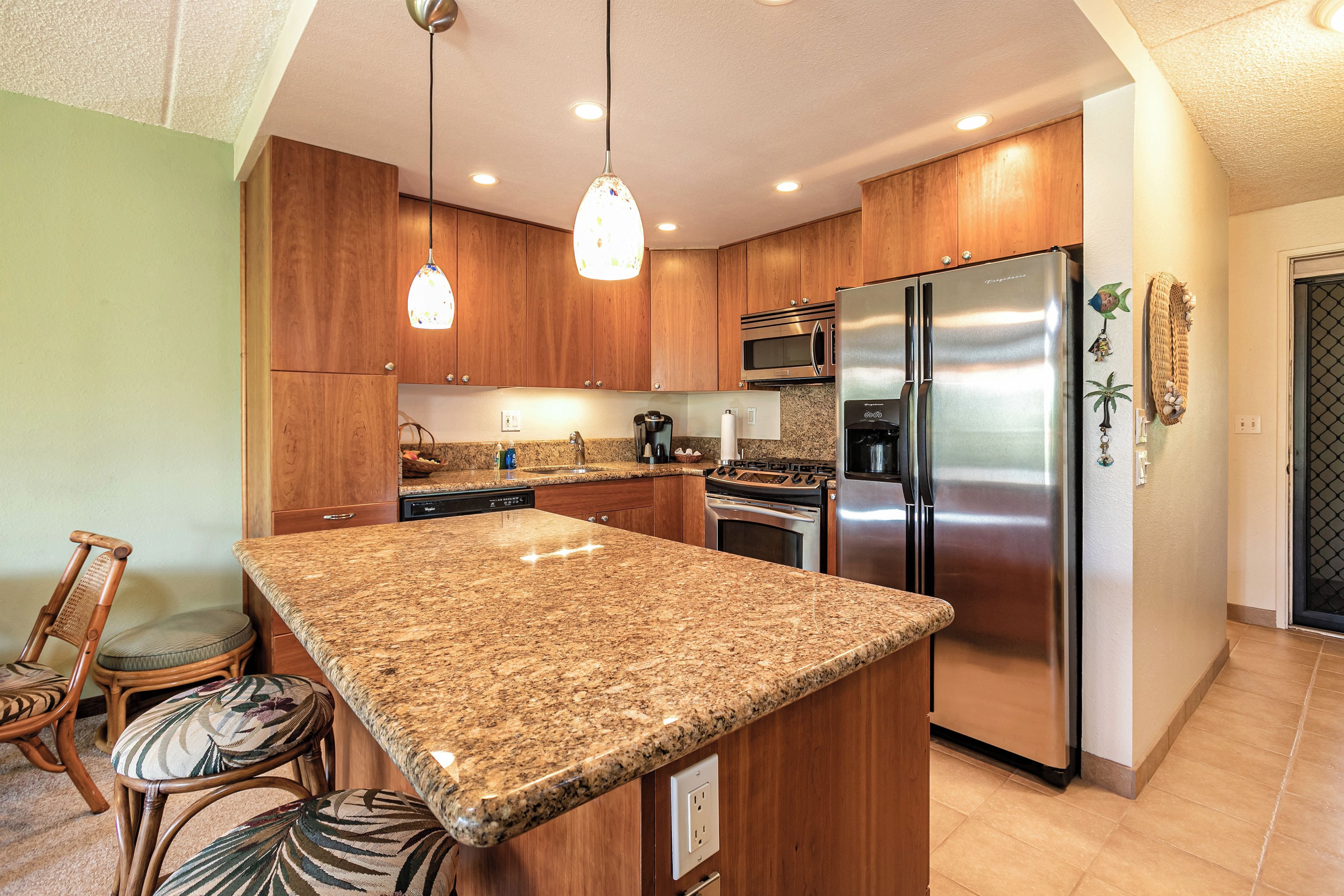 Una cocina con encimeras de granito, armarios de madera, electrodomésticos de acero inoxidable y una zona de comedor con sillas de mimbre.