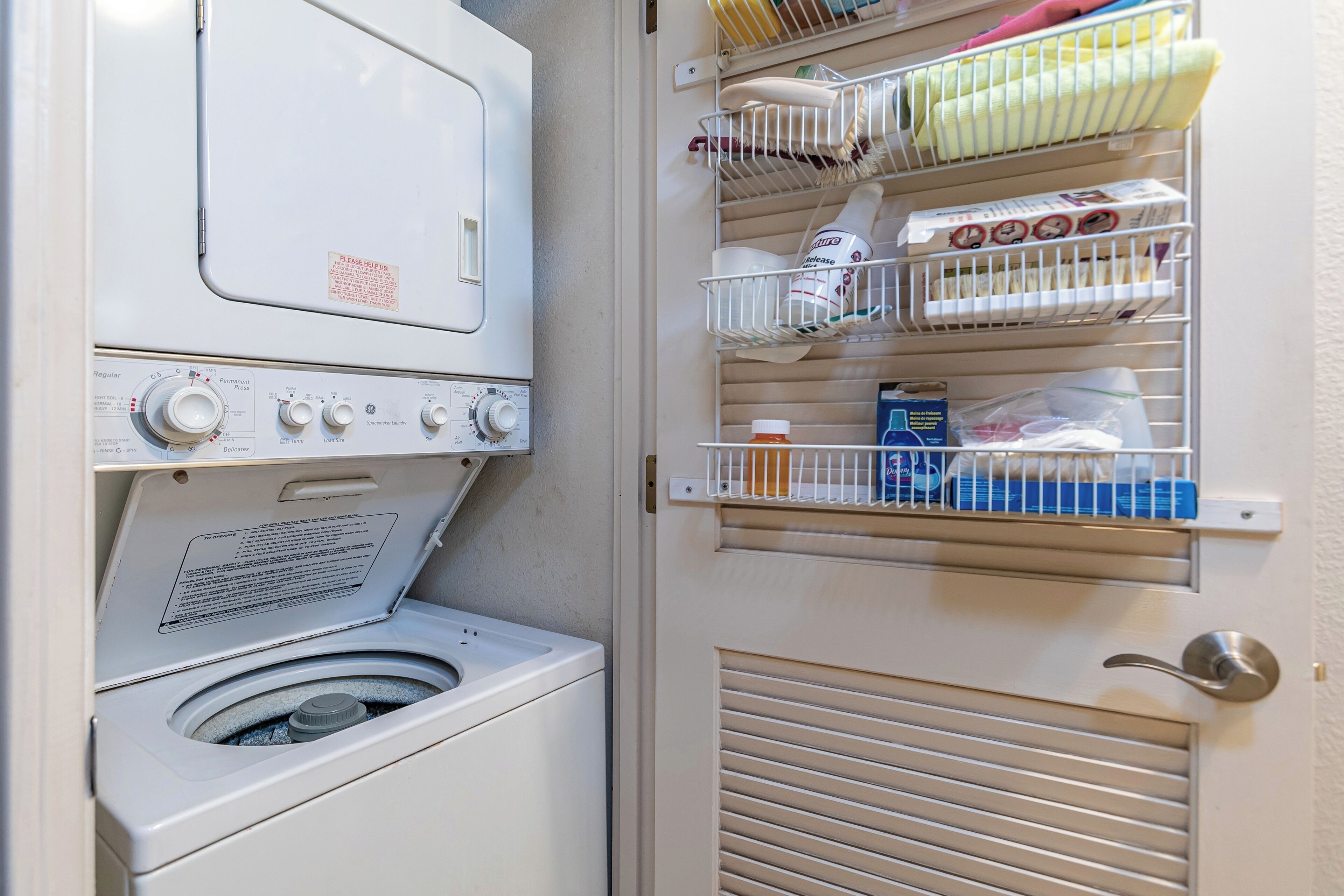 A laundry room with a front-loading washer and dryer, shelves with folded laundry, and storage bins.