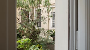 Blick durch eine offene Tür auf ein Gebäude mit Gartenanlage, einschließlich verschiedener Pflanzen und einem Fenster mit Gitterstäben.