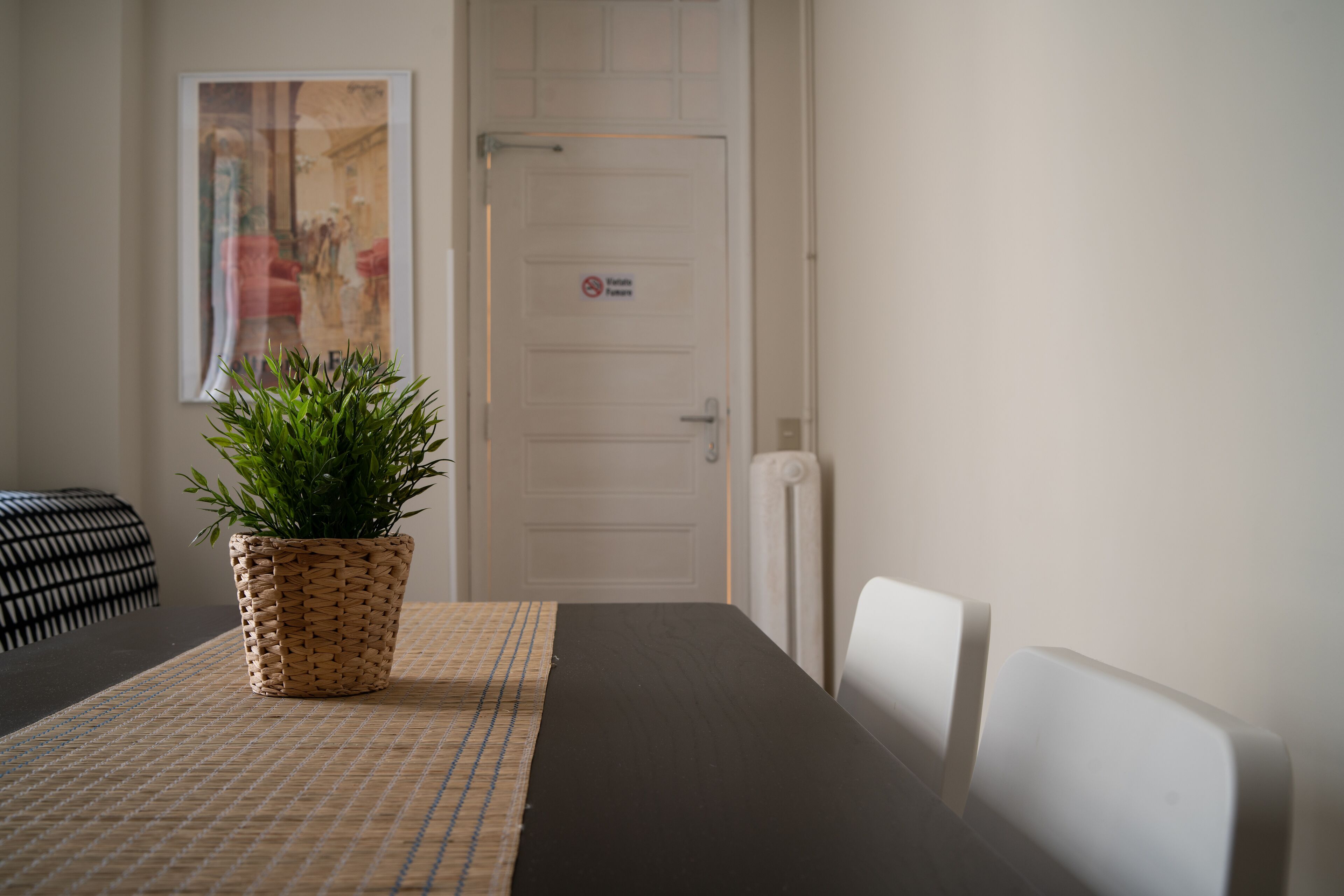 Ein Zimmer mit einem dunklen Holztisch, einem gewebten Blumentopf und einer weißen Tür mit einem 'Nichtraucher'-Schild.