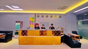 A reception area with a yellow counter, three staff members, a refrigerator, and a window with a view. - Mandalay Hill View Inn (Mandalay)