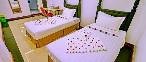 A hotel room with two single beds, each with a green headboard and white bedding. There is a small table with a chair and a mirror on the wall.