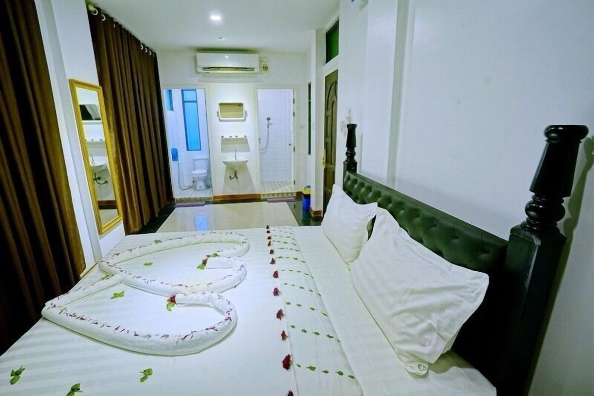 Une chambre d’hôtel avec un lit, un miroir, une salle de bain visible au fond et une fenêtre.