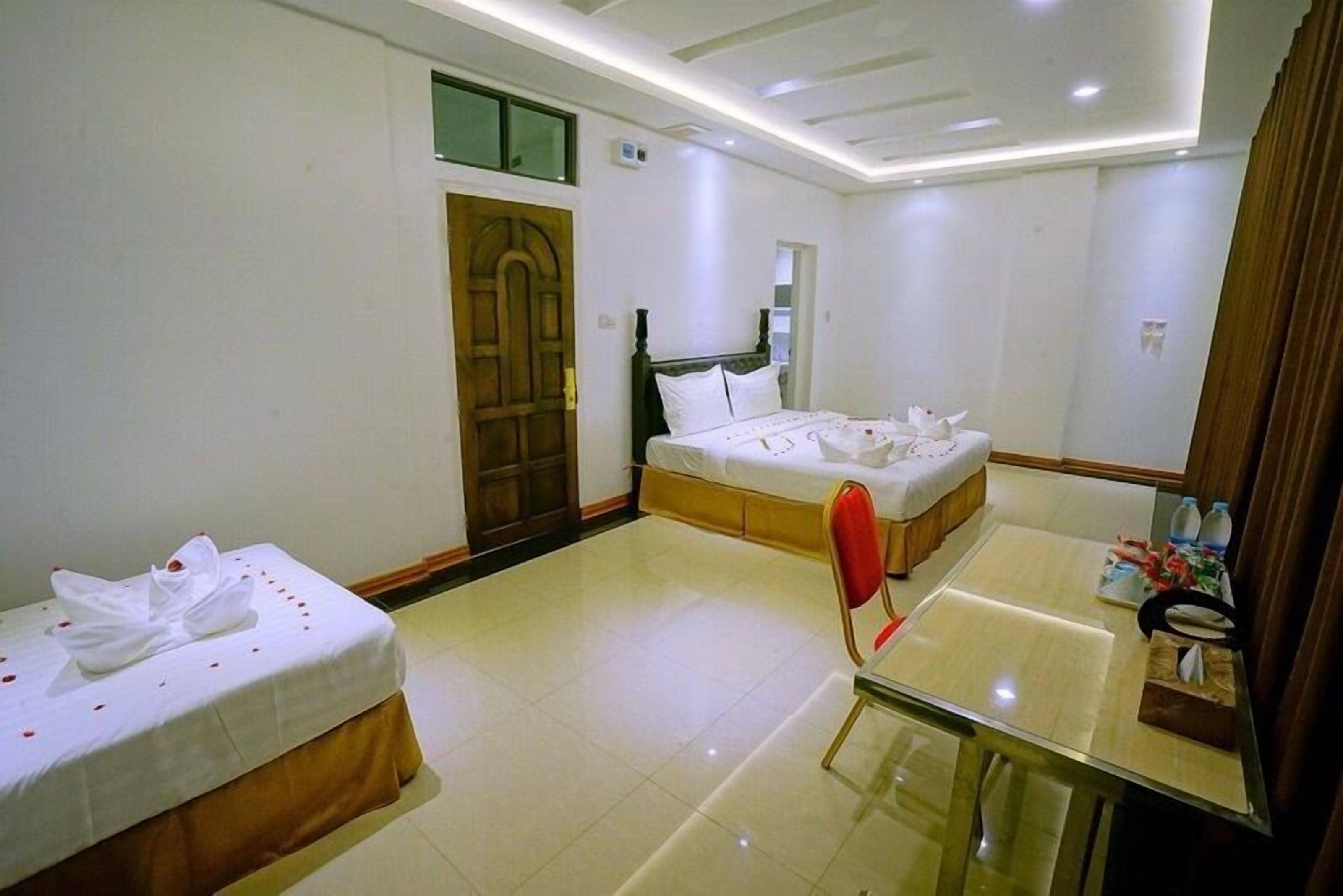 A hotel room with two beds, a wooden door, a mirror, a glass table, and a small table with toiletries.