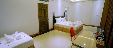 A hotel room with two beds, a wooden door, a mirror, a glass table, and a small table with toiletries.