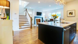 A modern kitchen with a central island, wooden flooring, and a staircase leading to another level. - Close to Broadway · Rooftop Skyline · Walkable (Nashville)