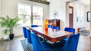 A spacious dining area with a large wooden table, blue upholstered chairs, and a modern chandelier. - Close to Broadway · Rooftop Skyline · Walkable (Nashville)