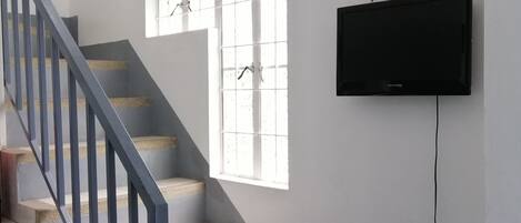 A staircase with a blue railing leading to a landing. A window with white bars is visible on the landing wall.