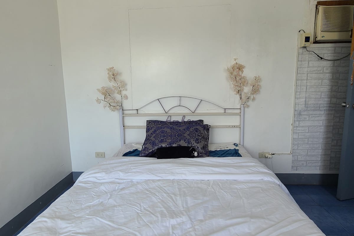 A bedroom with a single bed, a headboard with a floral design, and a wall-mounted air conditioner.