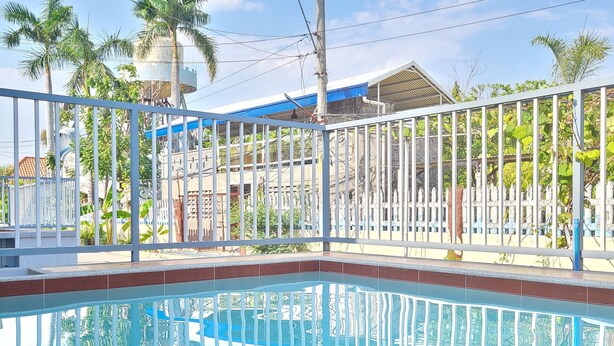 Una piscina con ringhiera metallica, circondata da palme e un edificio con tetto blu.