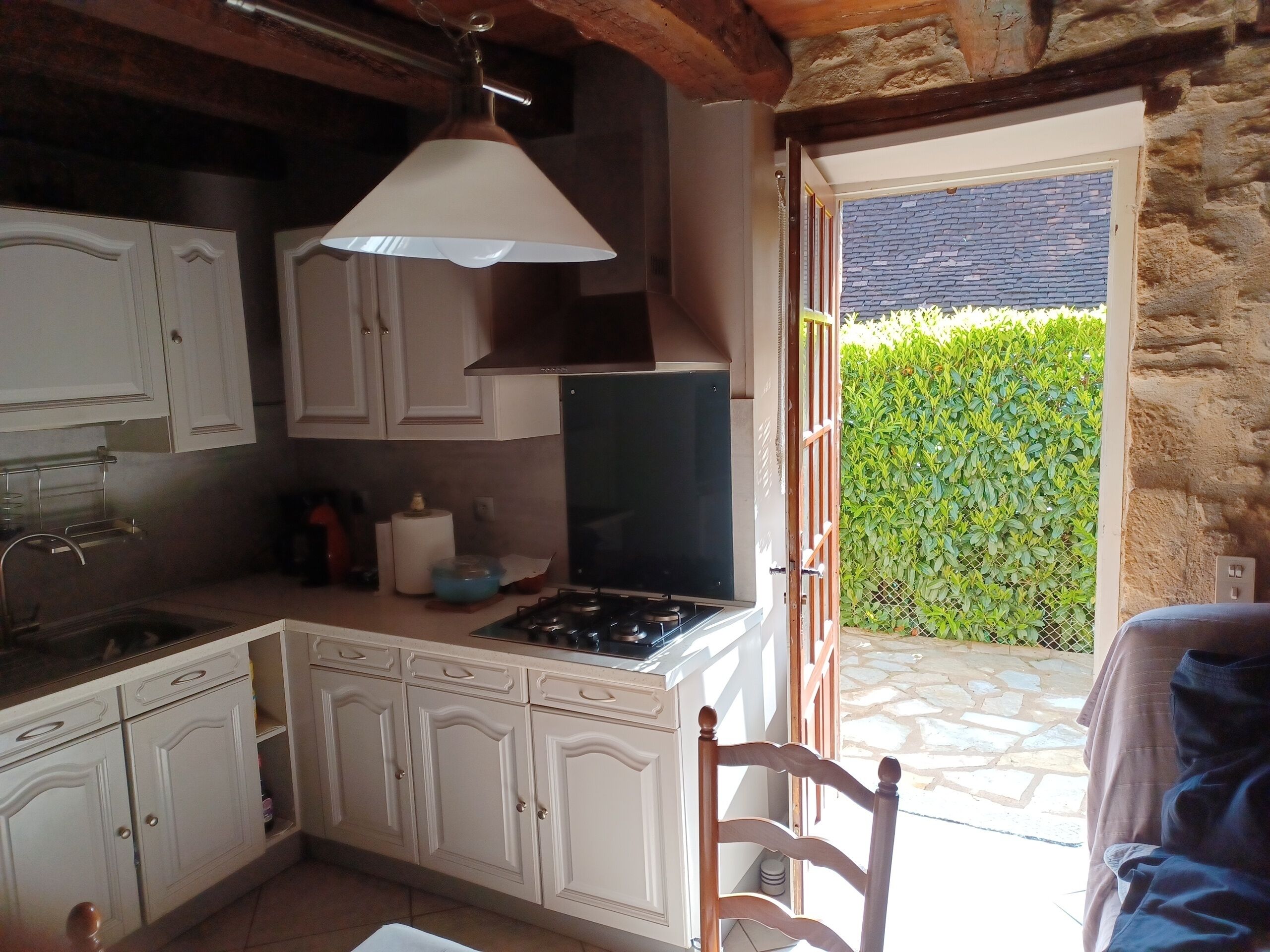 Una cocina compacta con armarios blancos, estufa a gas y lámpara colgante.