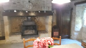 A dining area with a stone fireplace, wooden chairs, and a table with a vase of flowers. - Country house in the heart of Black Périgord (Dordogne)