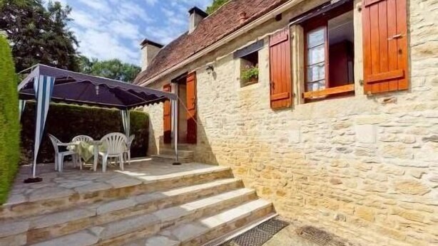 A stone building with a porch, steps leading to the entrance, and a covered outdoor seating area with chairs. - Country house in the heart of Black Périgord (Dordogne)