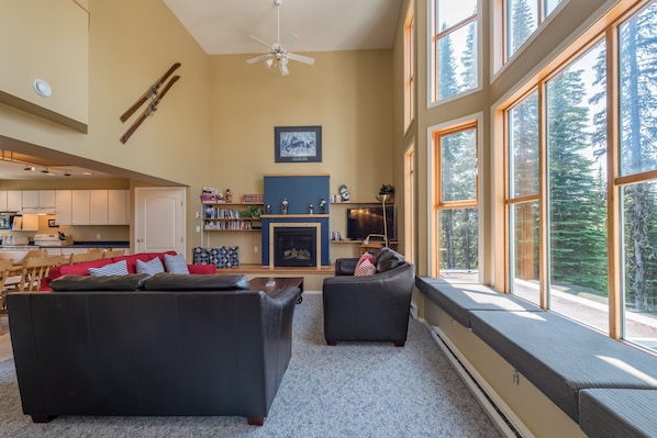 Relax in a spacious living area with a fireplace, TV, and bookshelf, offering a forest view.