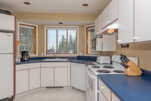 Compact kitchen with a corner layout, featuring a refrigerator, microwave, toaster, and stove with four burners, sink, and dishwasher.