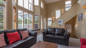 A spacious living room with large windows, a staircase, and a fireplace. - Amazing location right on the ski way - bright home with private hot tub (Silver Star Mountain)