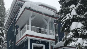 A two-story building with a balcony, surrounded by snow-covered trees. - Amazing location right on the ski way - bright home with private hot tub (Silver Star Mountain)
