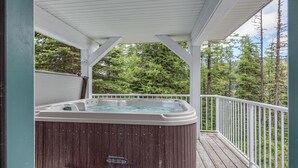 A hot tub on a wooden deck with a white railing, surrounded by trees. - Amazing location right on the ski way - bright home with private hot tub (Silver Star Mountain)