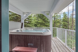 Relax in a hot tub on a deck surrounded by lush greenery.