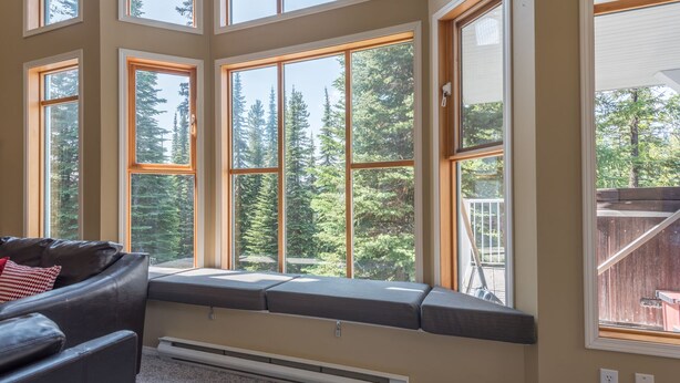 A room with large windows, a built-in bench, and a view of trees. - Amazing location right on the ski way - bright home with private hot tub (Silver Star Mountain)
