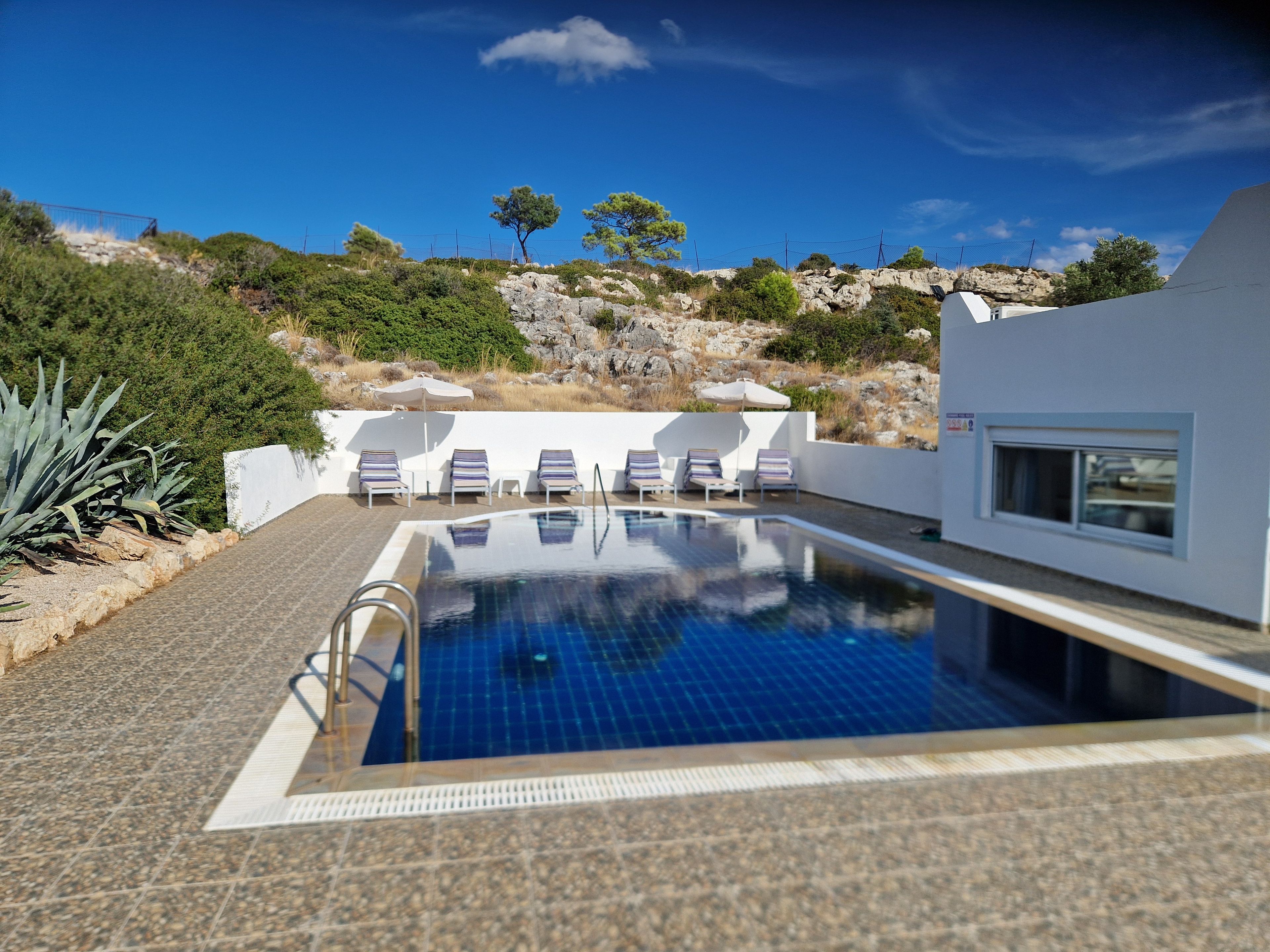 A swimming pool with lounge chairs, a stone pathway, and a view of a rocky hillside.
