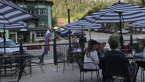 Uteservering med parasoller, utsikt över bergen och en byggnad med en grön fasad.