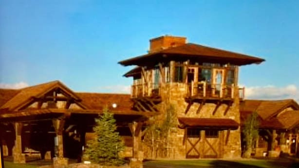 En stor, rustik lodge med ett centralt torn, flera skorstenar och en rymlig veranda.