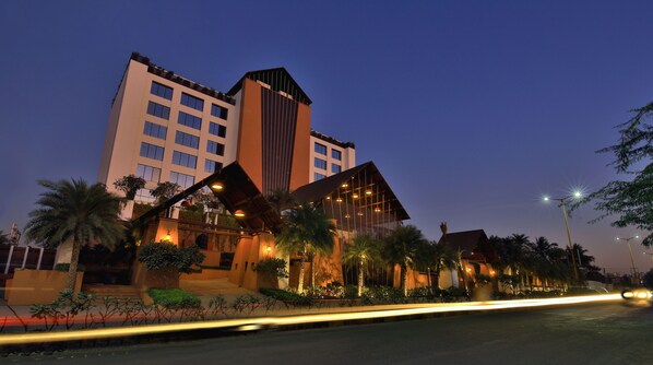 A modern hotel with a prominent tower, multiple balconies, and well-lit outdoor areas.
