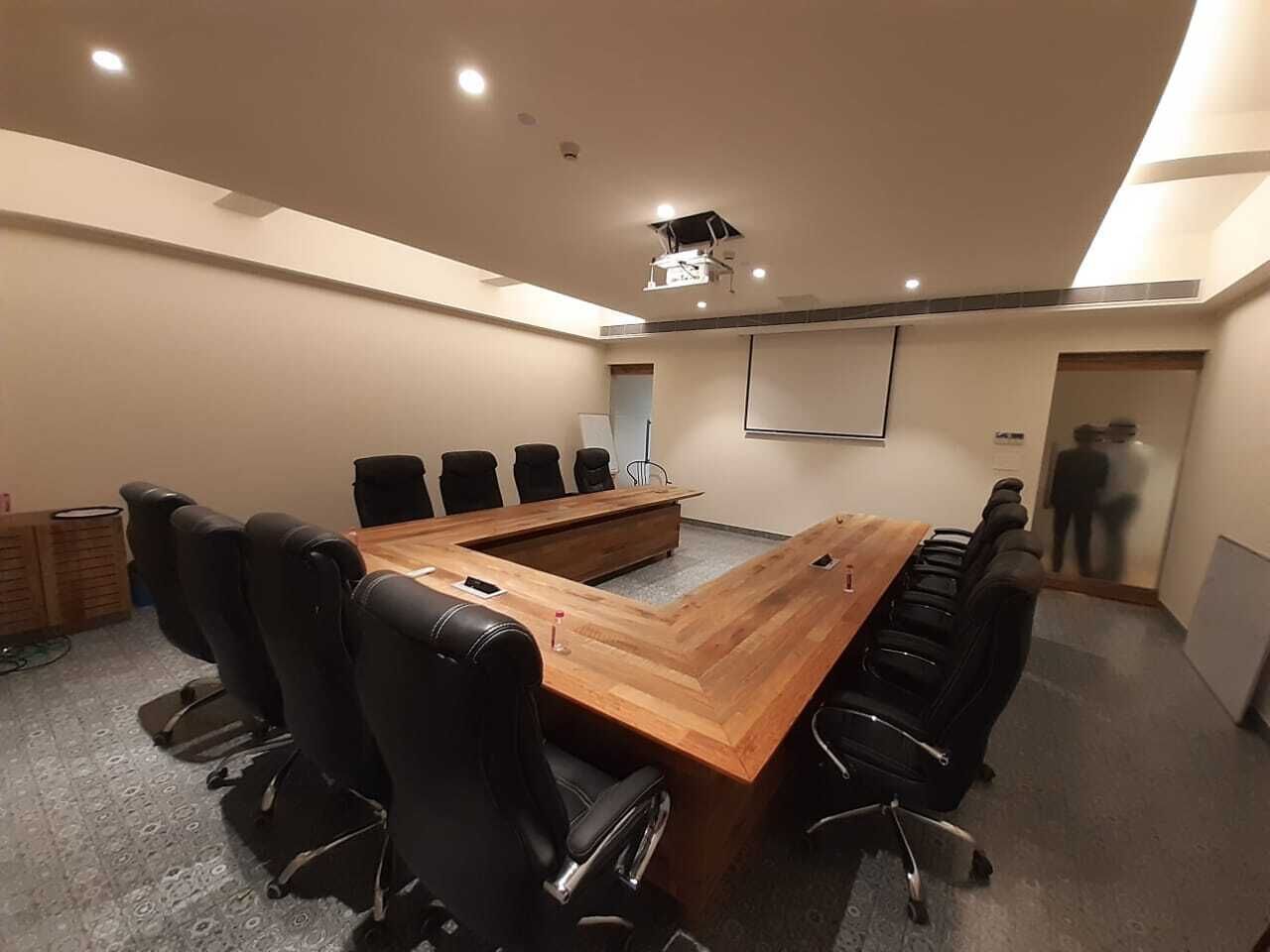 A conference room with a long wooden table, black chairs, and a projector screen.