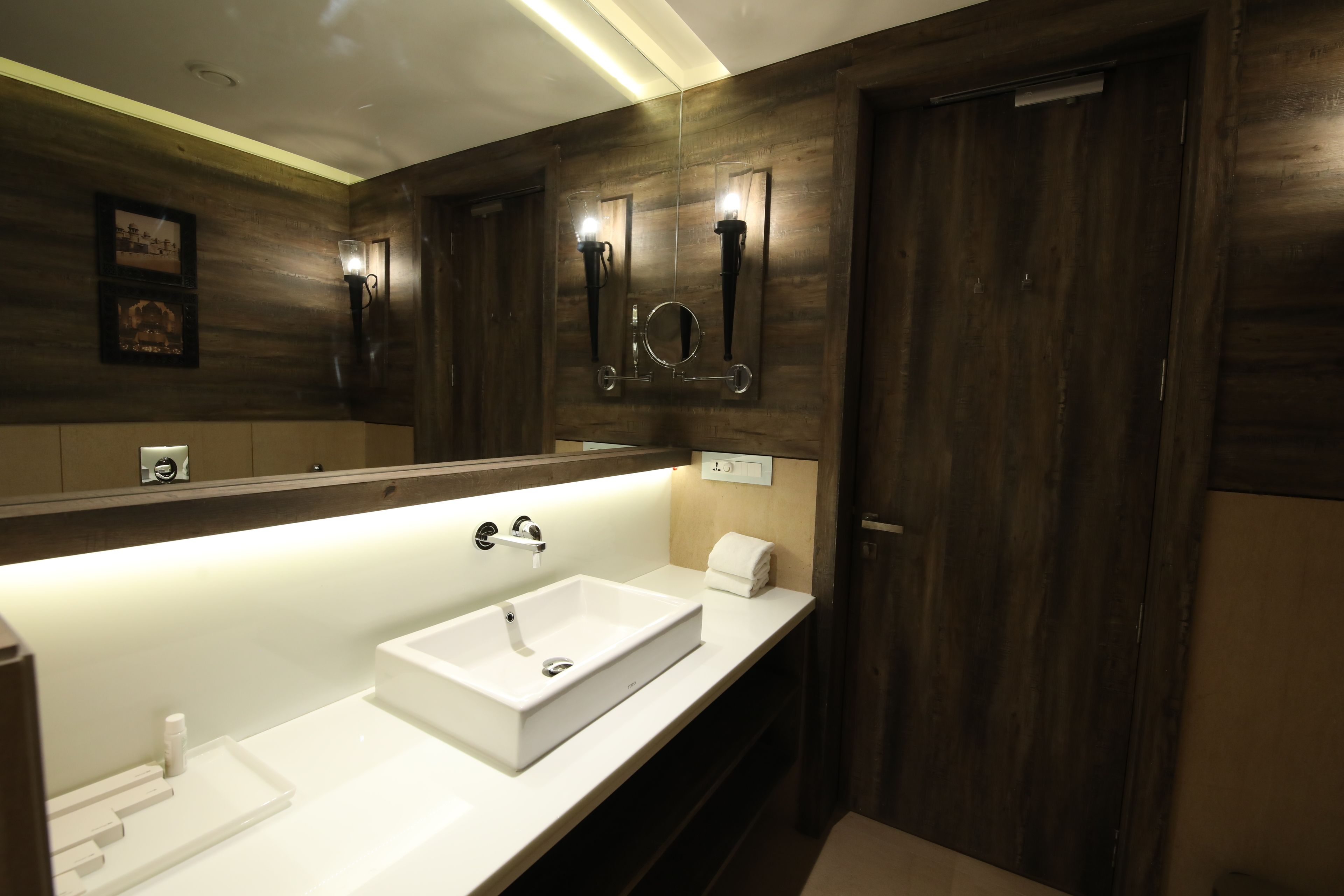A modern bathroom with a large mirror, a white sink, and wooden paneling.
