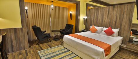 Una habitación de hotel con una cama grande, dos sillones, una mesita y un espejo.
