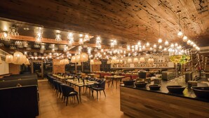 A restaurant with multiple dining areas, wooden ceiling, and various hanging light fixtures.
