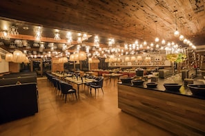 A restaurant with multiple dining areas, wooden ceiling, and various hanging light fixtures.