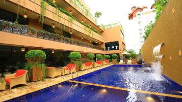 Zona de piscina de hotel con piso de baldosas azules, sillas de descanso y una cascada.
