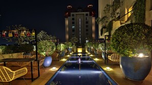 A rooftop pool area with lounge chairs and potted plants, surrounded by a building with balconies. - Sayaji Rajkot (Rajkot)
