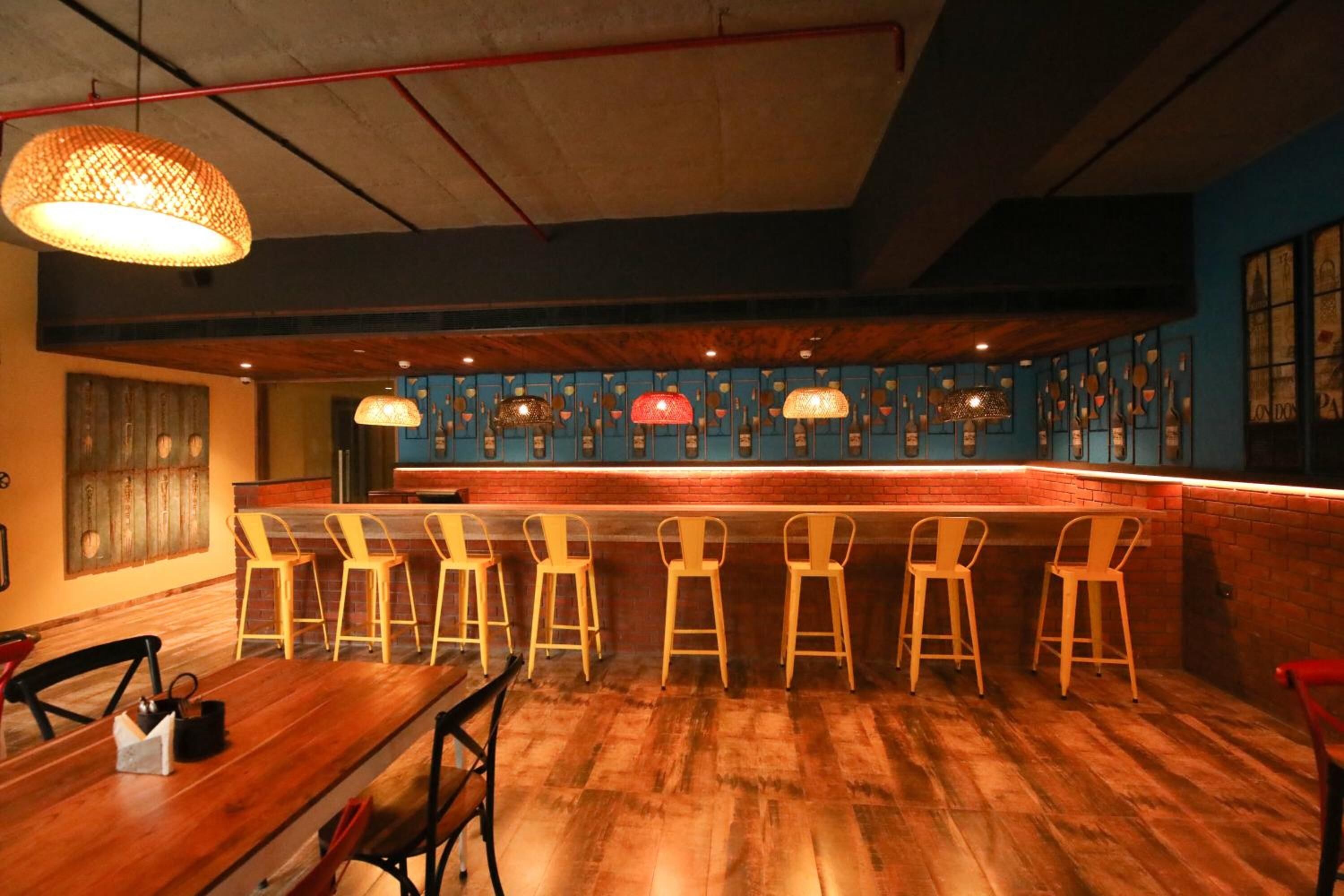 Un área de bar con suelo de madera, una barra larga y varias sillas amarillas.