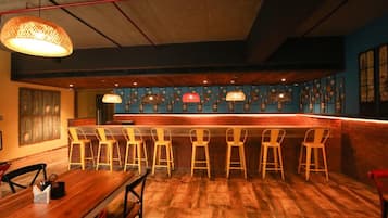 Un área de bar con suelo de madera, una barra larga y varias sillas amarillas.