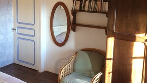 Una habitación con piso de madera, una silla de mimbre, una estantería y una puerta con cinta azul.