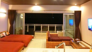 Habitación de hotel con dos camas, un sofá, un televisor y un balcón con cortinas.